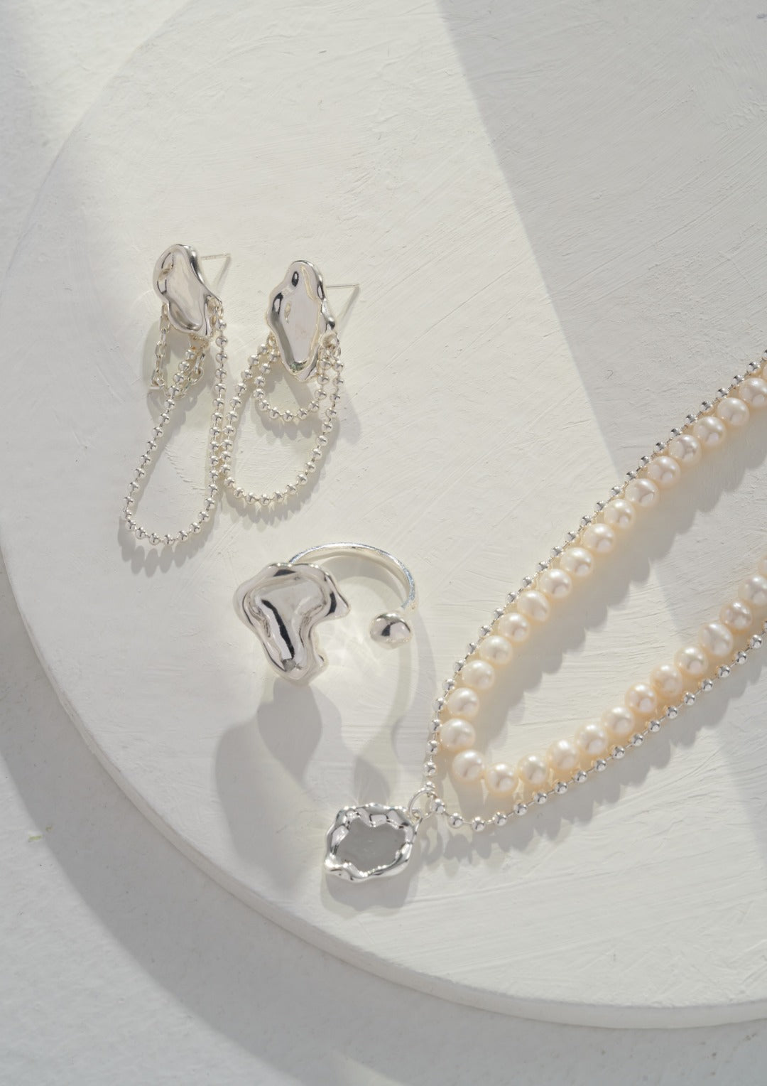 A white plate with a silver necklace adorned with freshwater pearls, along with earrings and a ring.