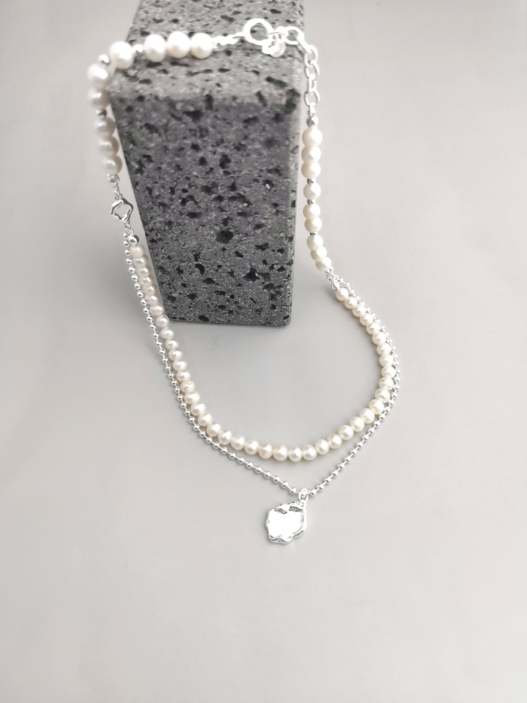 Elegant silver necklace featuring disc-shaped pearl charm, styled with freshwater pearls.