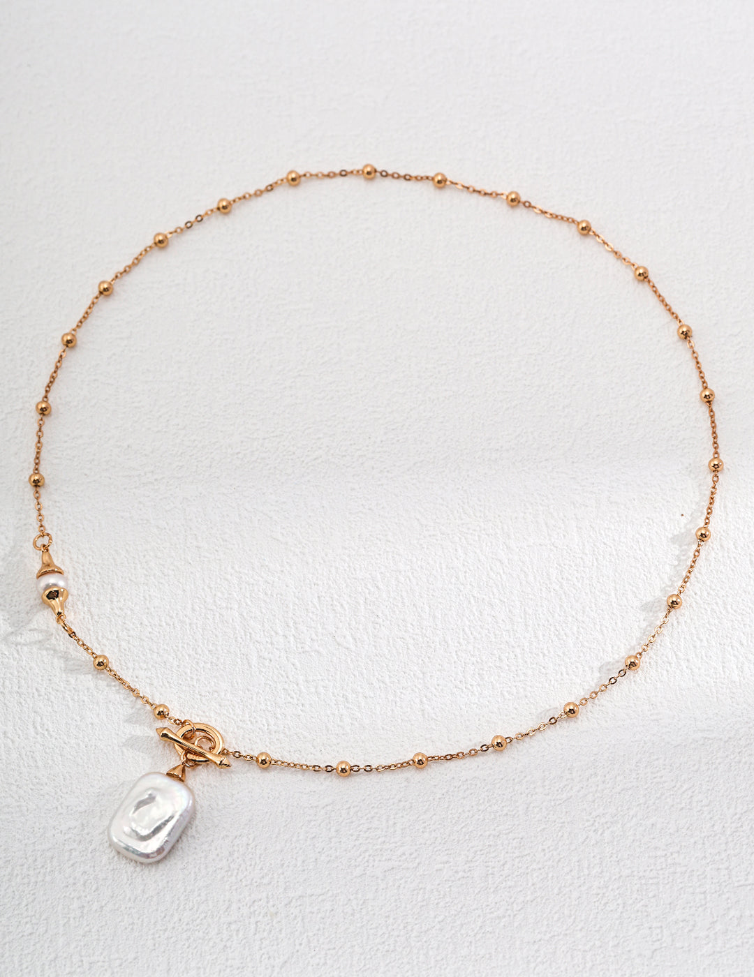Elegant gold chain bracelet with dotted charms, showcasing square freshwater pearl pendant on chain.