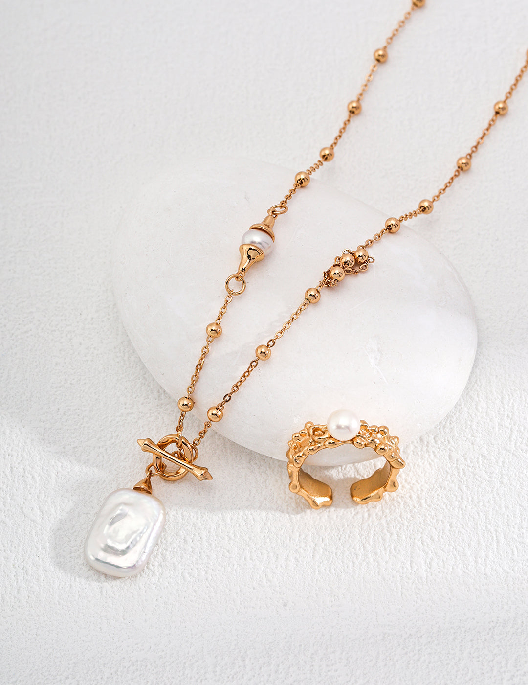 Dainty gold necklace adorned with square freshwater pearl pendant on dotted chain, accompanied by matching ring.