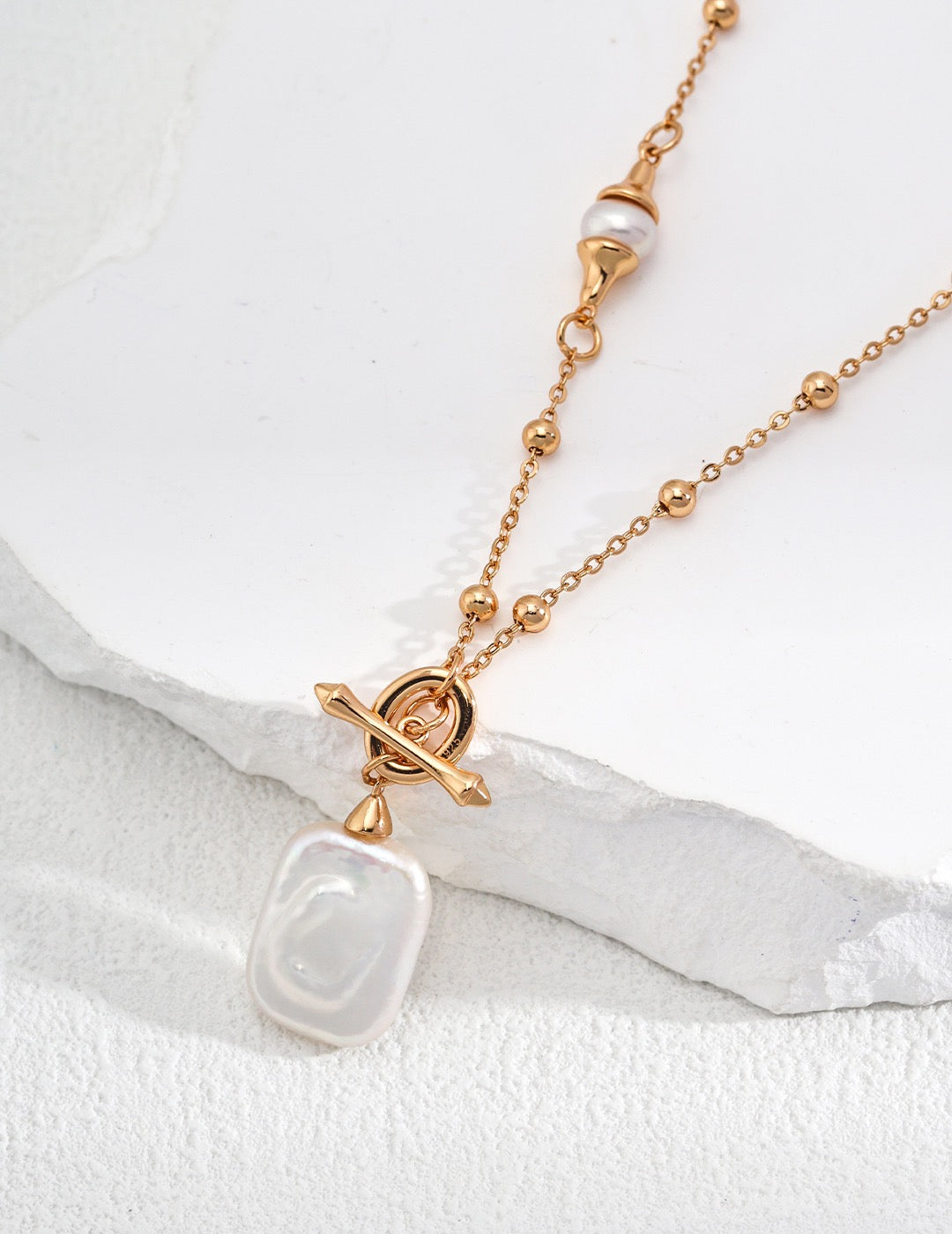 Gold dotted chain necklace with elegant pearl pendant from Mezuille, leaning on white sculpture.