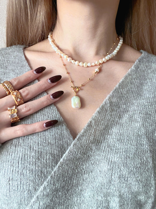 A woman adorned with a pearl necklace and several rings, exuding sophistication and charm.