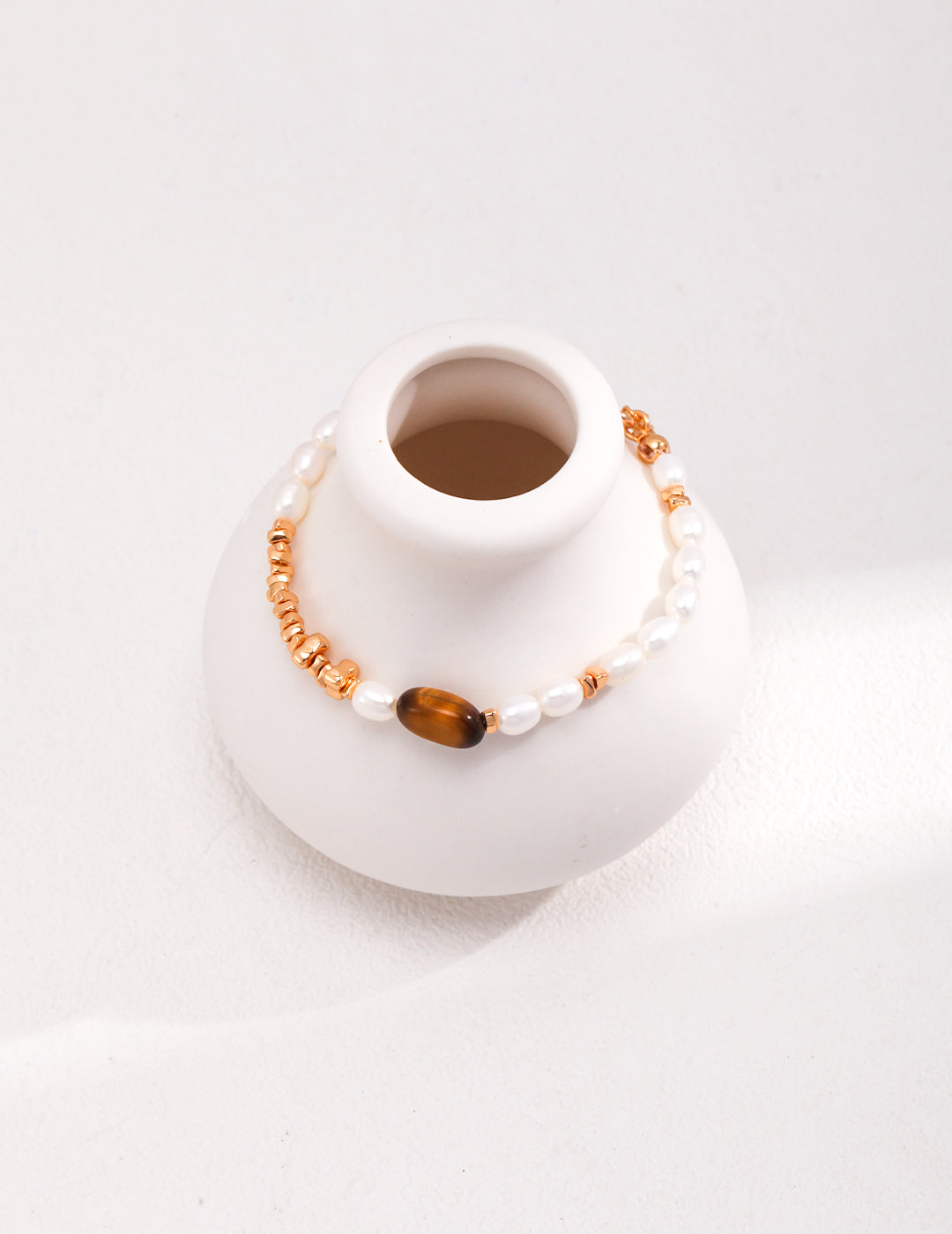 Decorative white vase featuring a stunning tiger's eye and pearl gold bracelet.