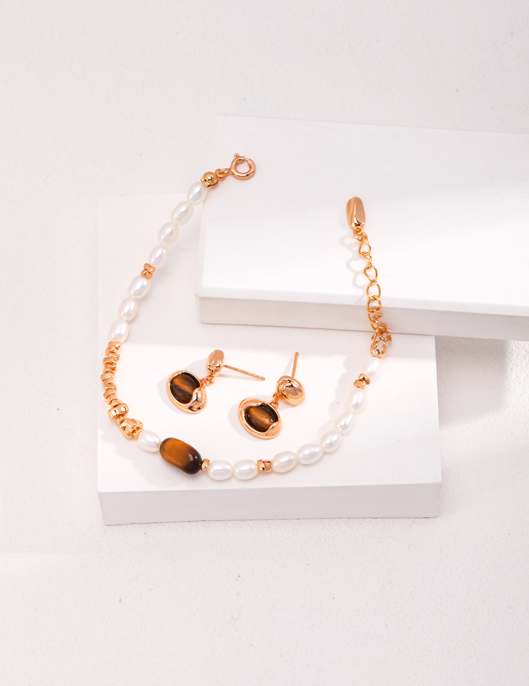 A beautiful combination of tiger's eye and pearl jewelry set, featuring earrings and a bracelet, showcased on a white surface.