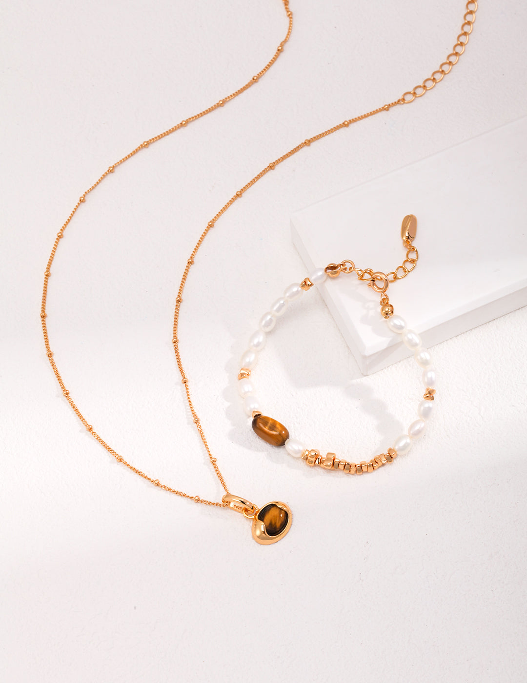 A luxurious gold necklace and bracelet set featuring a dainty gold chain, embellished with tiger's eye and pearls.