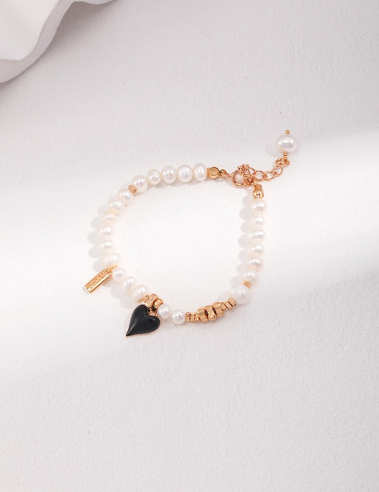 A stunning bracelet with pearls, adorned with gold beads and black heart charm.