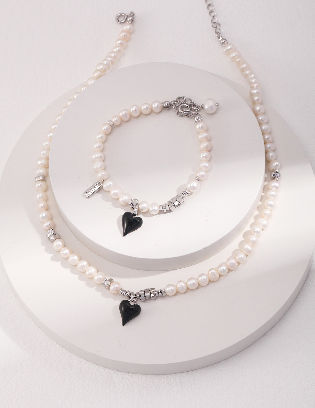 Stylish white pearl necklace featuring silver chain and black enamel heart pendant.