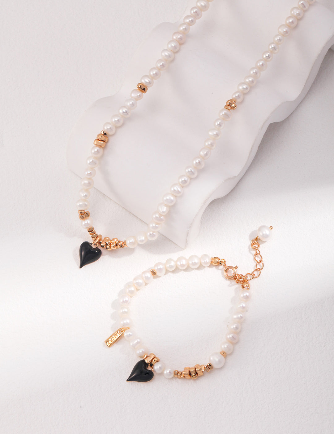 A stunning gold and pearl necklace and bracelet set with a black enamel heart pendant, perfect for any elegant occasion.