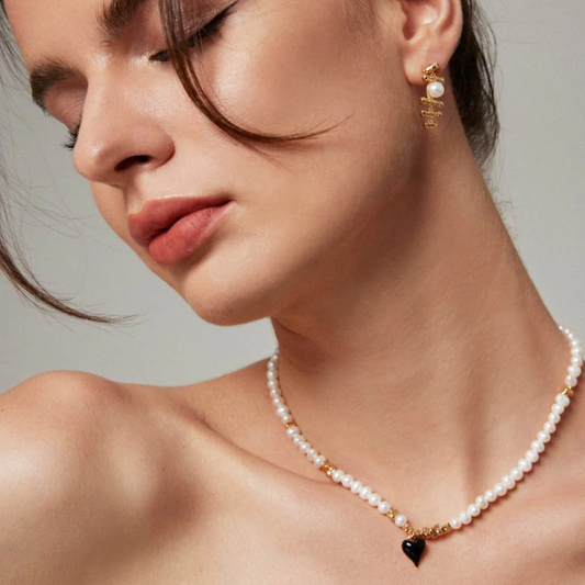 A woman models a gold heart necklace embellished with pearls.