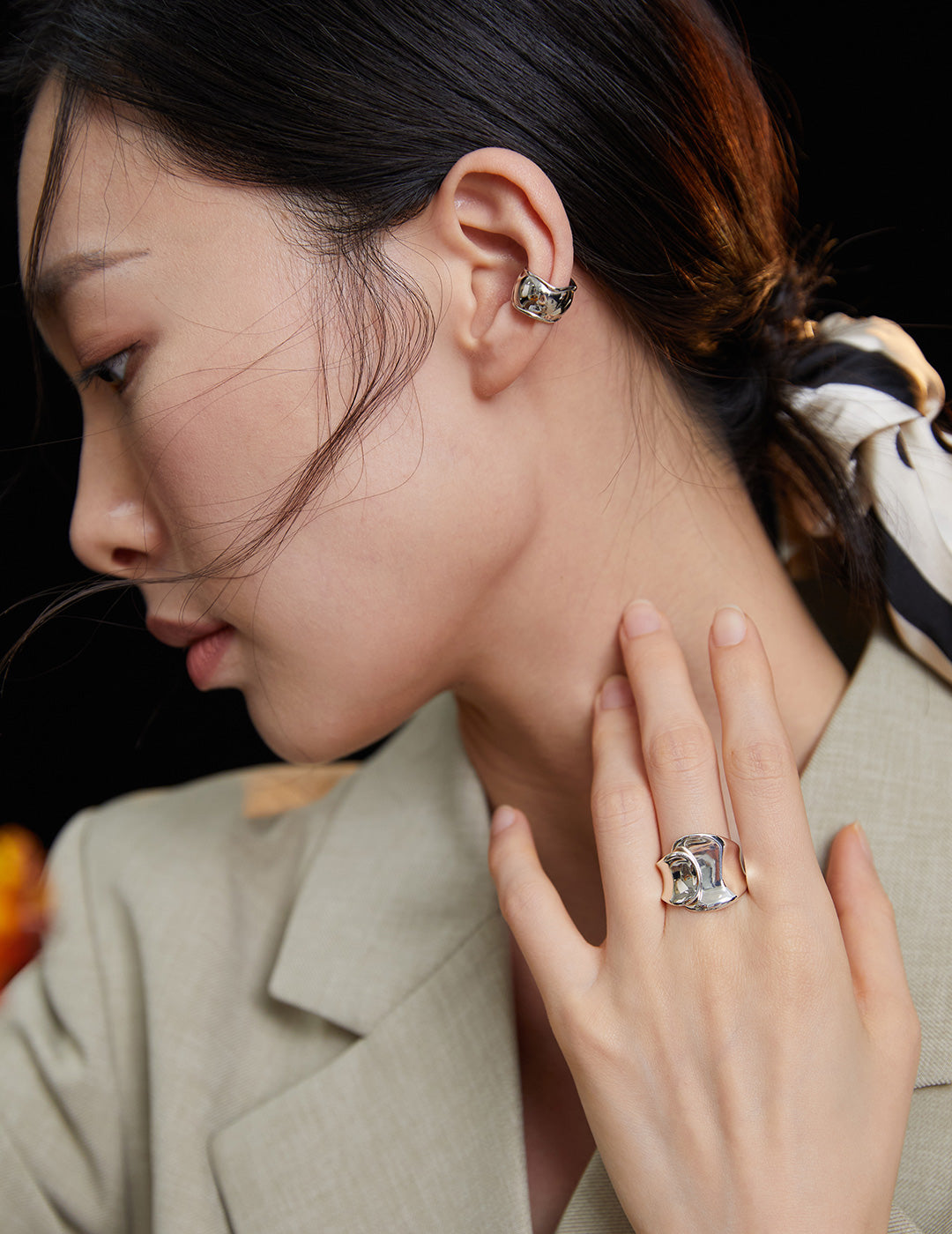 An elegant lady flaunting her silver accessories - a ring and earrings, featuring a trendy chunky belt ring.