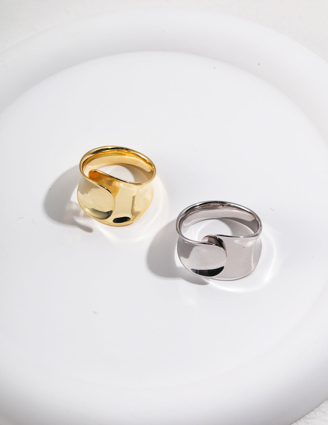 Two chunky belt rings, one gold and one silver, displayed on a white plate.