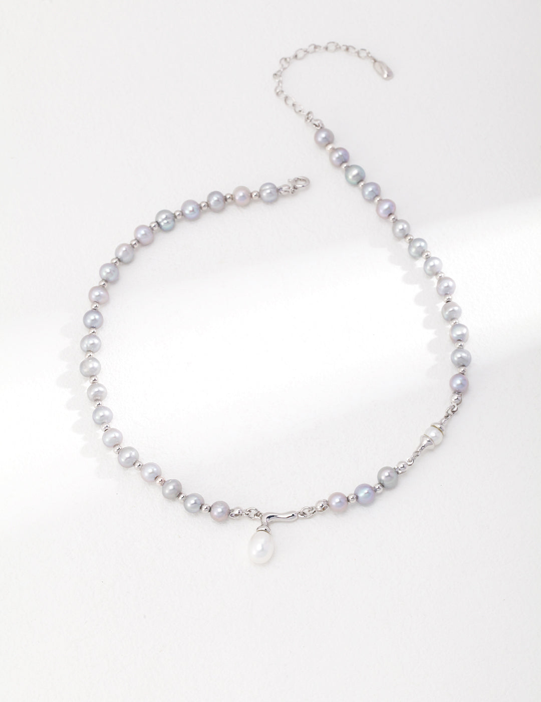 A silver necklace with a delicate pearl pendant, showcasing grey freshwater pearls.