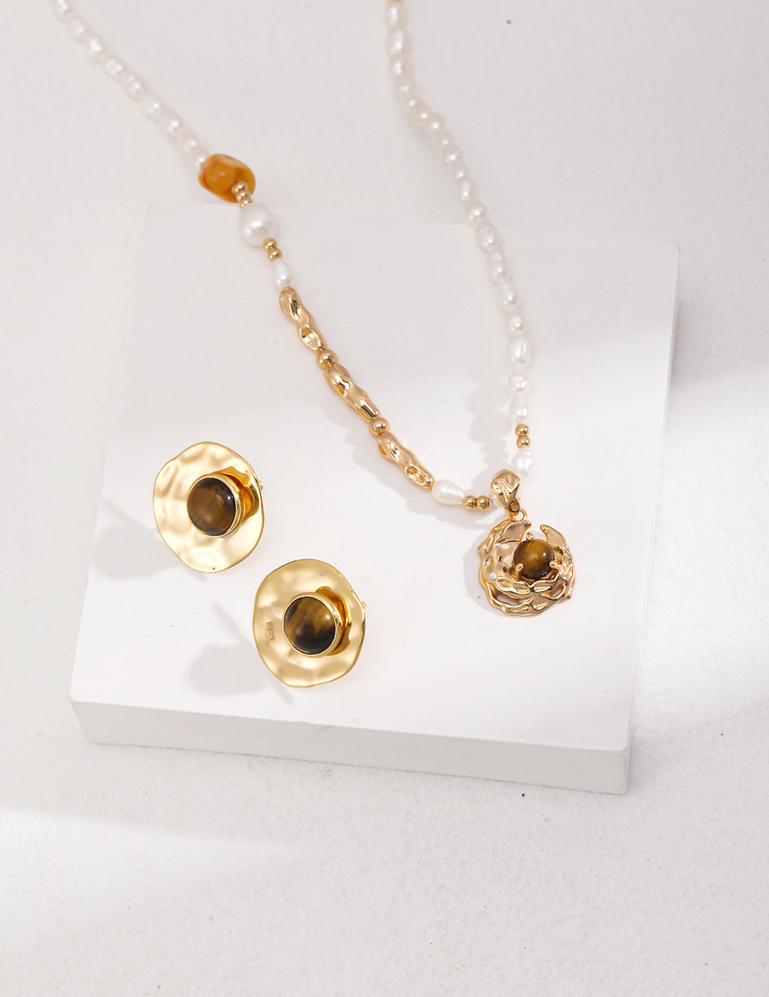 Luxurious gold necklace and earrings set with pearl and tiger's eye crescent moon design on white background.