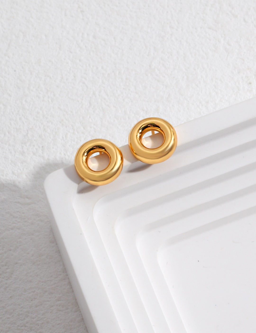 Pair of gold donut earrings on white plate.