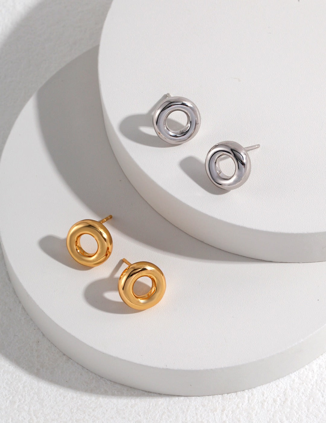 Two pairs of donut earrings in gold and silver on a white surface.