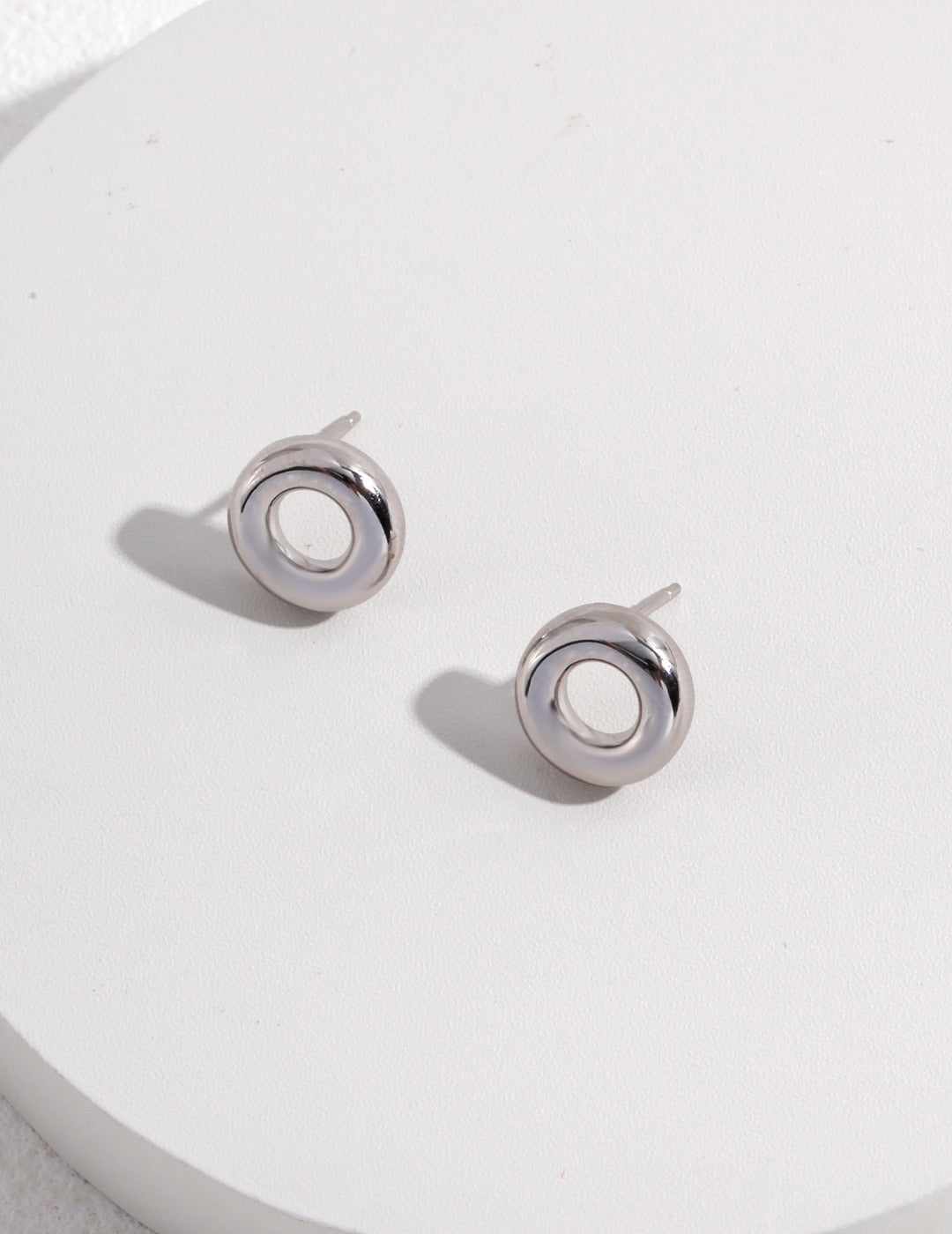 Shiny silver donut earrings on white.