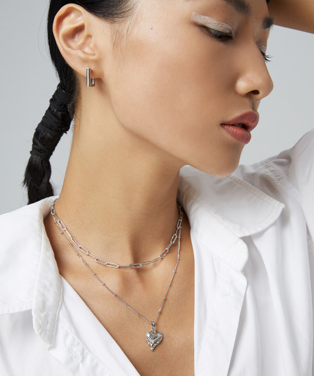 Woman in white shirt with silver chain necklace featuring heart charm.