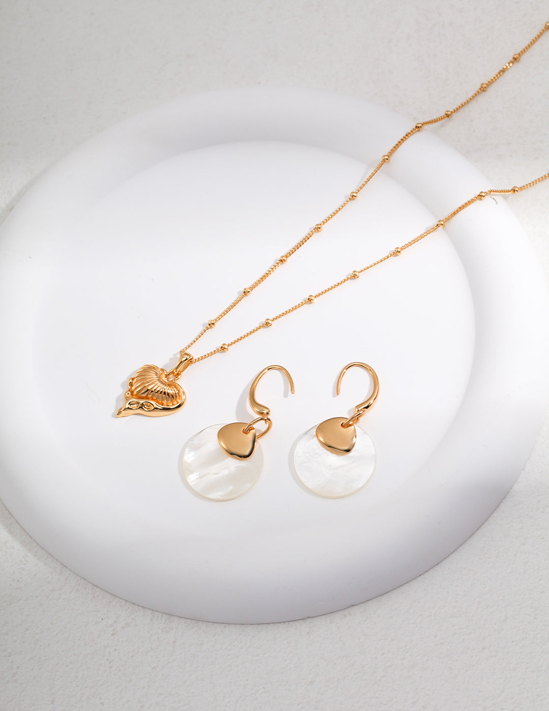 Stylish gold necklace and earrings arranged on white dish.