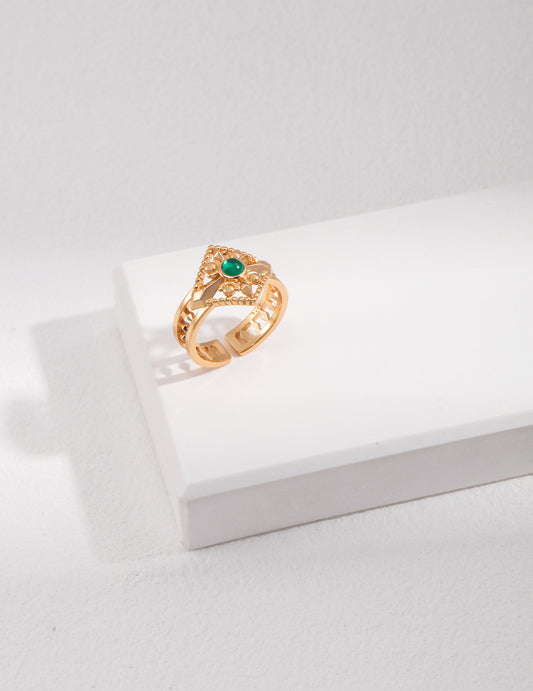 A retro gold ring with green cubic zirconia stones, placed on a white surface.