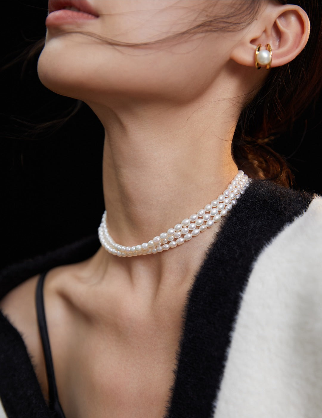 A model wearing a white sweater and a triple layer rice pearls necklace.