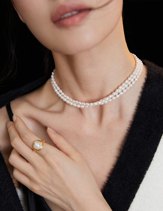 A woman wearing a triple layer rice pearls necklace and a matching pearl ring.