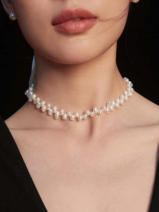 A woman elegantly dressed in a black dress, adorned with a stunning pearl choker necklace.