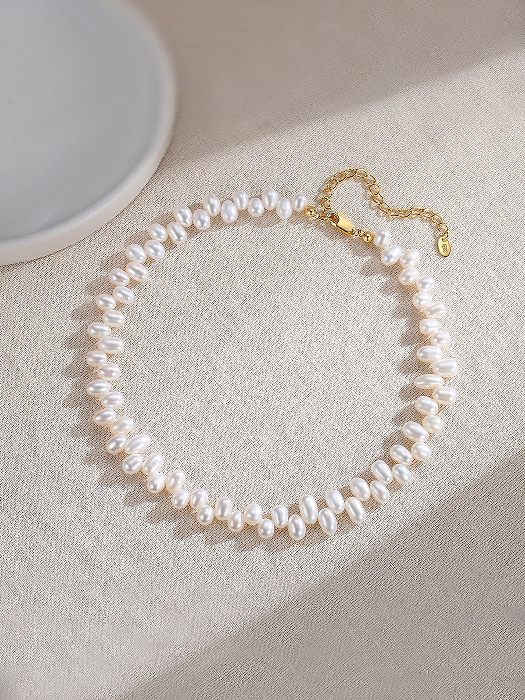 A delicate white pearl choker rests elegantly on a pristine white table, showcasing its timeless beauty.