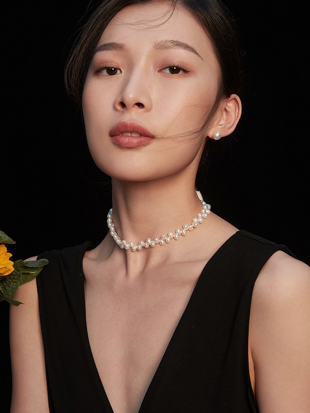 A stylish woman in a black dress, complemented by a chic pearl choker, radiating grace and charm.