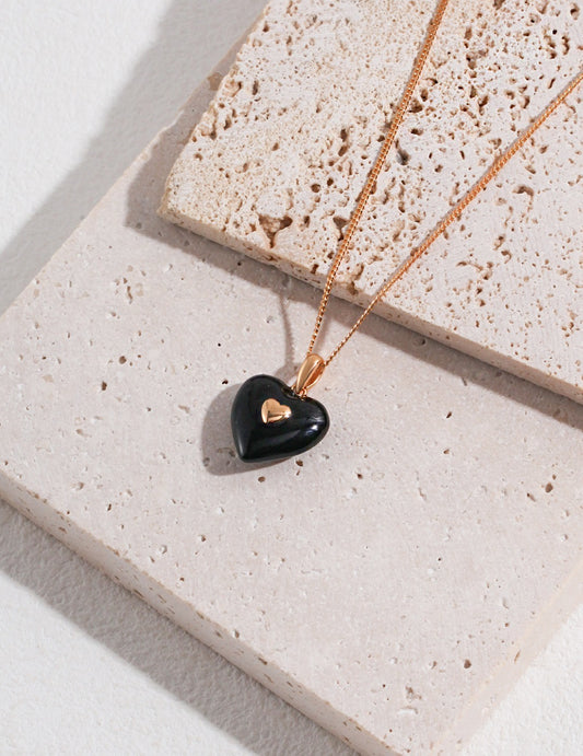 A stylish black heart necklace, lying on a stone surface, emphasizing its sleek appearance.