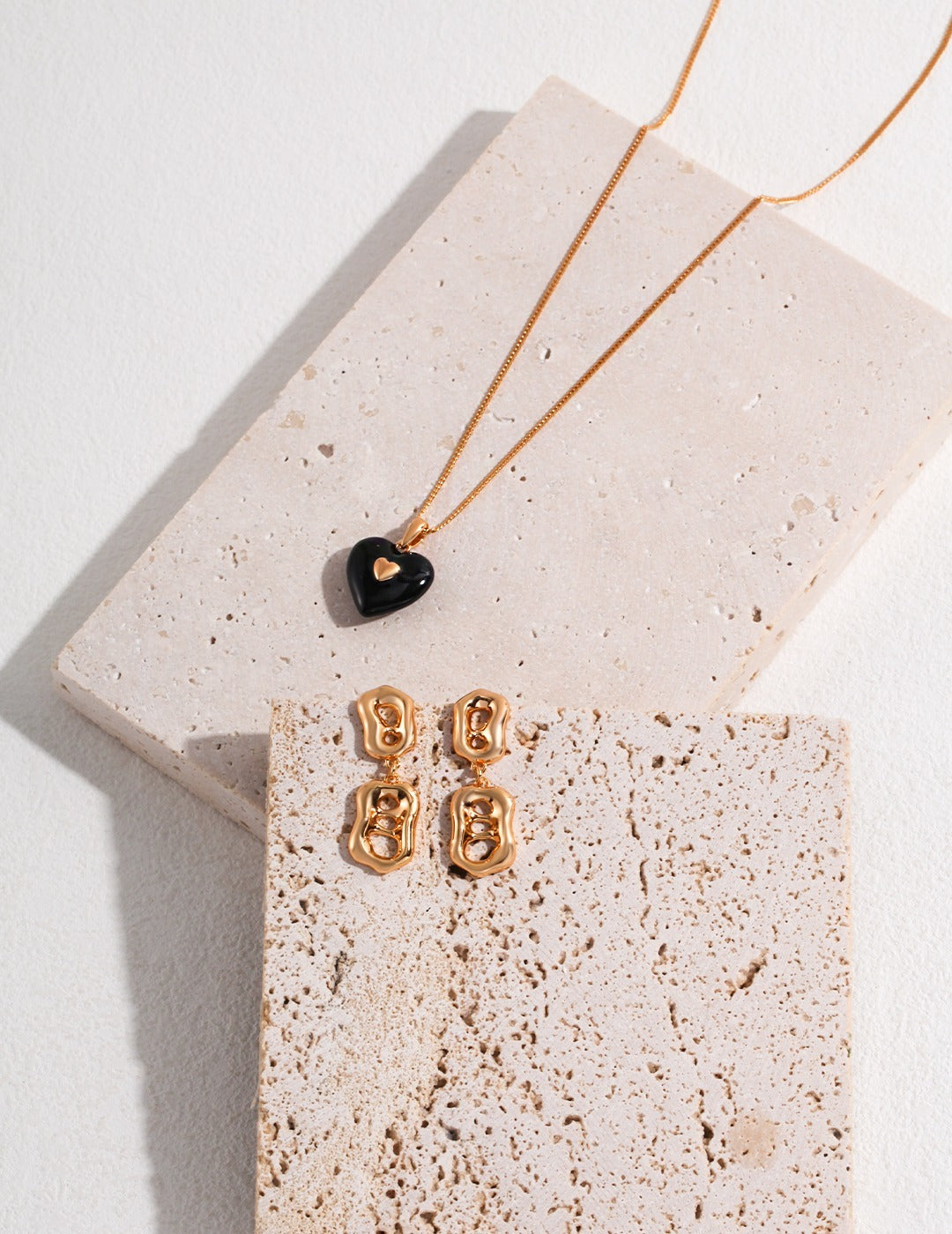 A stylish black heart necklace paired with earrings, beautifully arranged on a smooth white marble surface.
