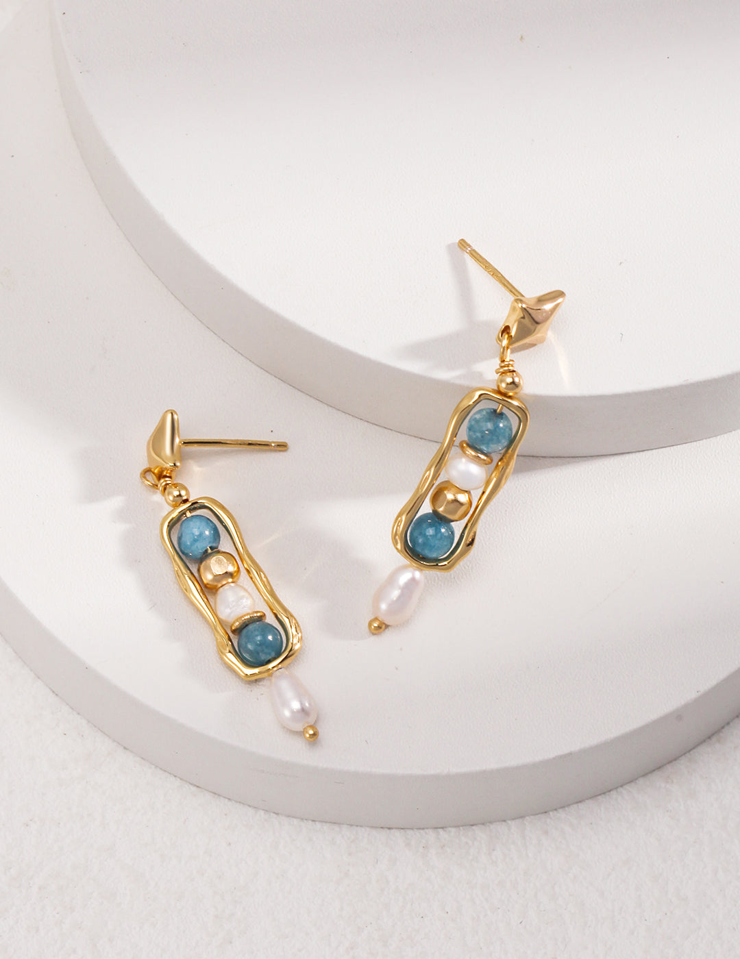 A pair of gold dangling earrings adorned with captivating gemstones, showcased on a pristine white surface.