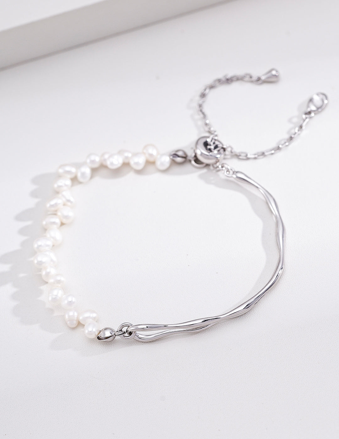 A close-up product photograph of the silver Emily Bracelet, highlighting its polished rhodium-plated architectural arch and the cascading strand of freshwater pearls.