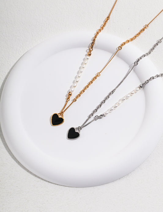 A white plate showcasing two necklaces with black heart charms - one gold, one silver - adorned with freshwater pearls.