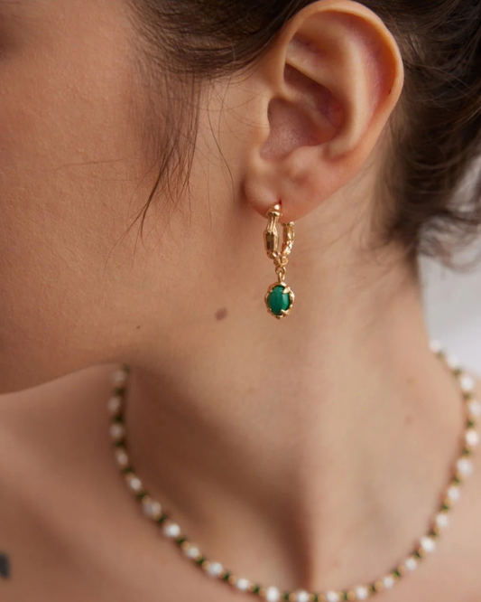 Close-up of a woman’s ear featuring malachite hoop earrings with gold and malachite accents.