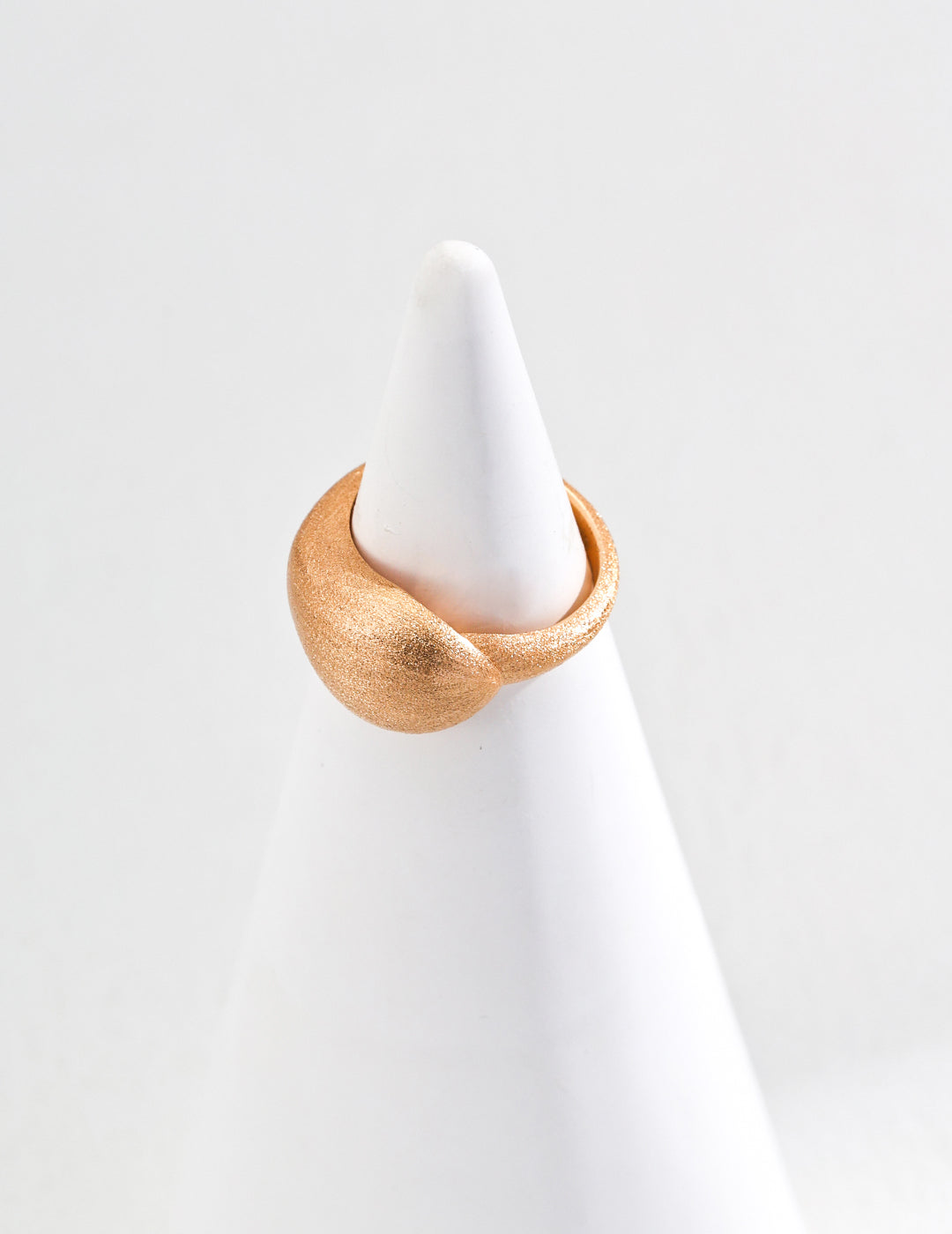 A matte gold ring elegantly placed atop a pristine white cone, showcasing a striking contrast in textures and colors.