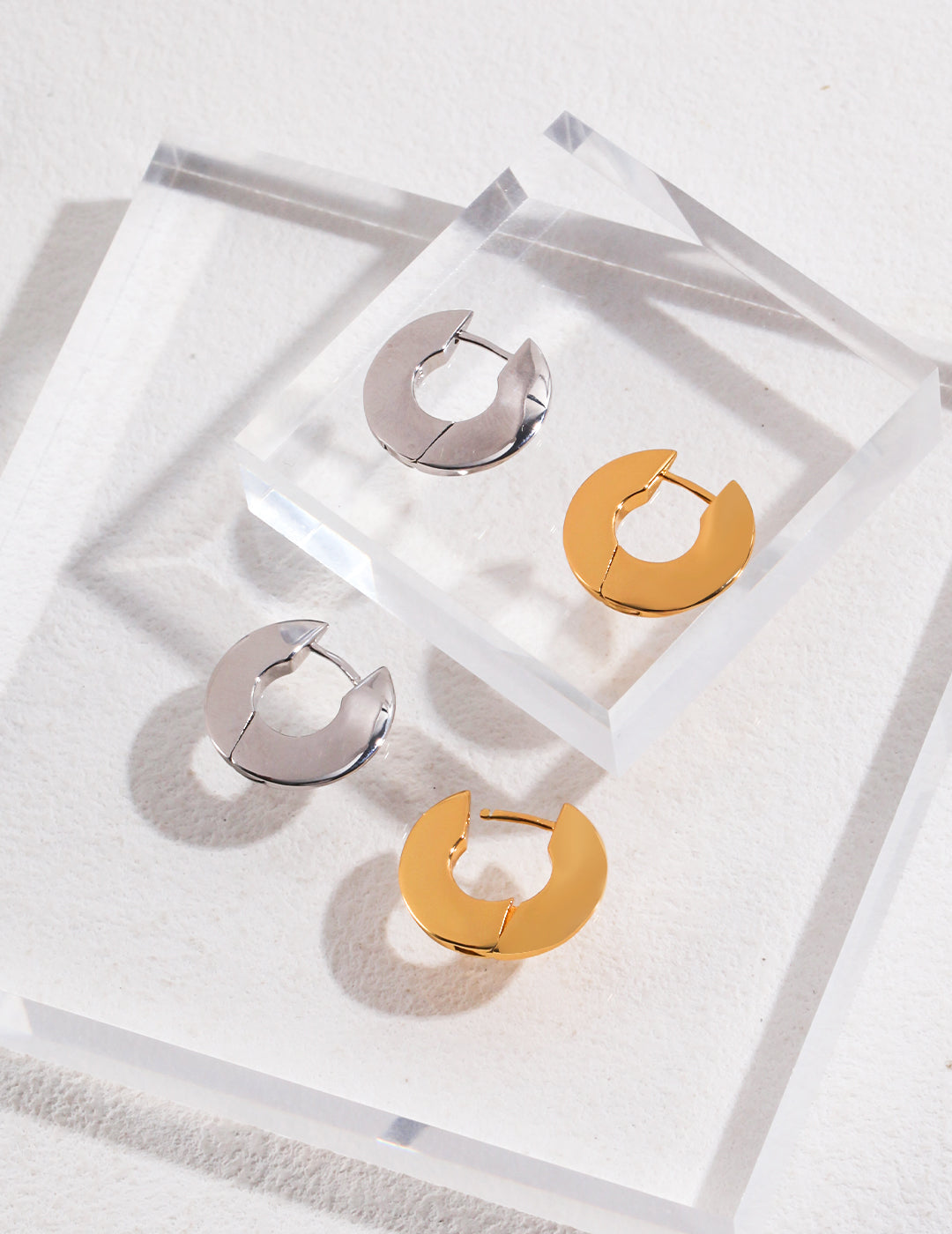 Two pairs of classic silver and gold hoop earrings on clear surface.