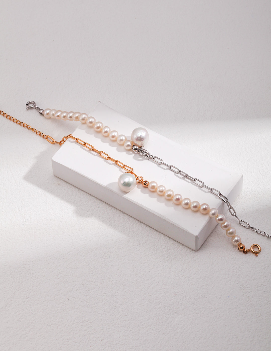 Two pearl bracelets, one silver and one gold, elegantly displayed on a white surface.