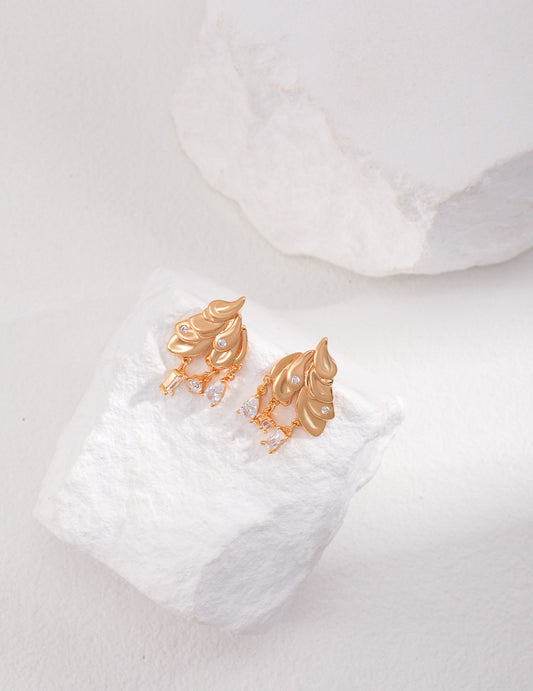 Gold earrings on white rock with feather details.