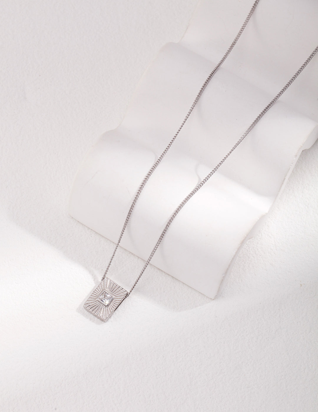 A silver necklace with a square pendant.