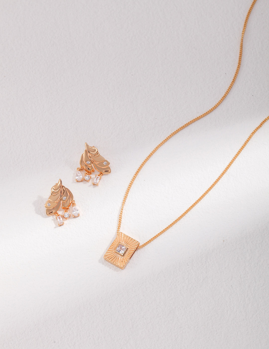 A gold necklace with a square pendant and matching earrings, perfect for adding elegance to any outfit.