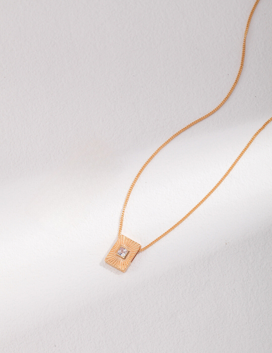 Shiny gold necklace adorned with square pendant.