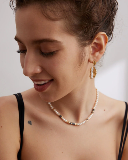 A woman models a black bra top paired with a Labradorite pearl necklace, highlighting her chic fashion choice.