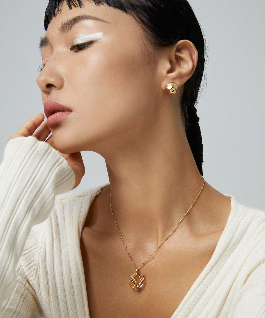 Fashionable woman wearing white sweater and gold necklace with robin pendant.