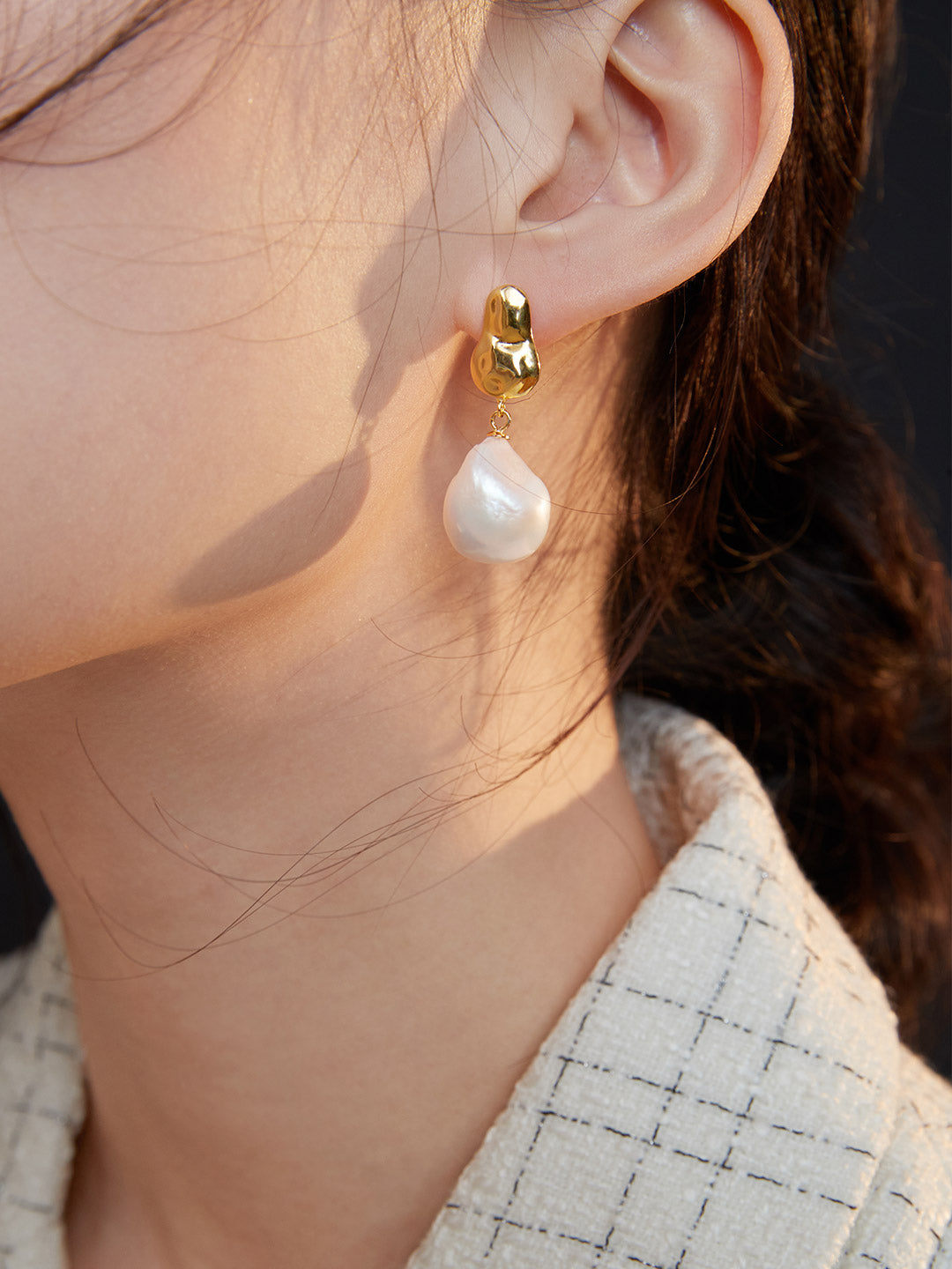 A model wearing gold baroque pearl drop earrings, adding elegance to her look.