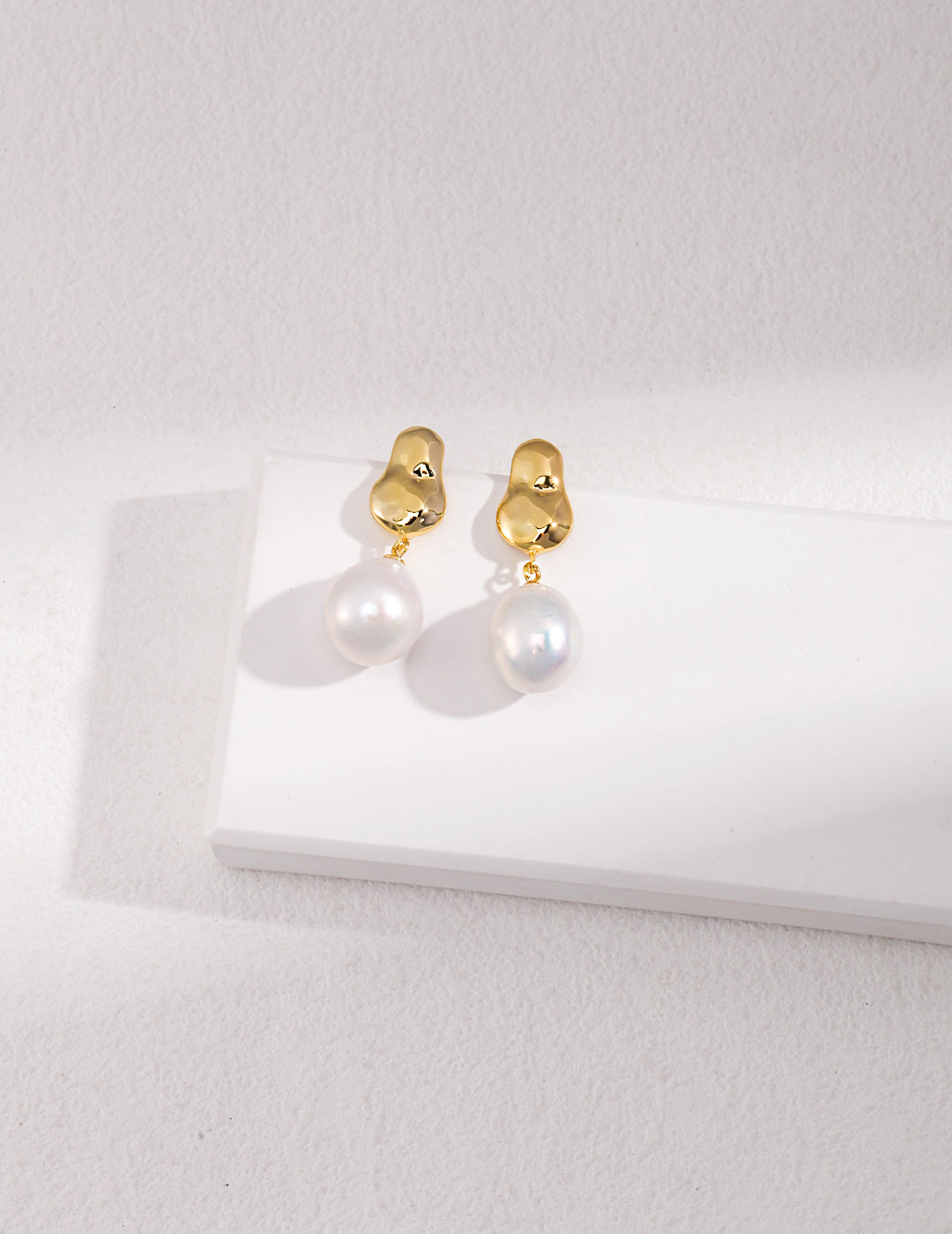 Stunning gold baroque pearl drop earrings showcased on a pure white surface.