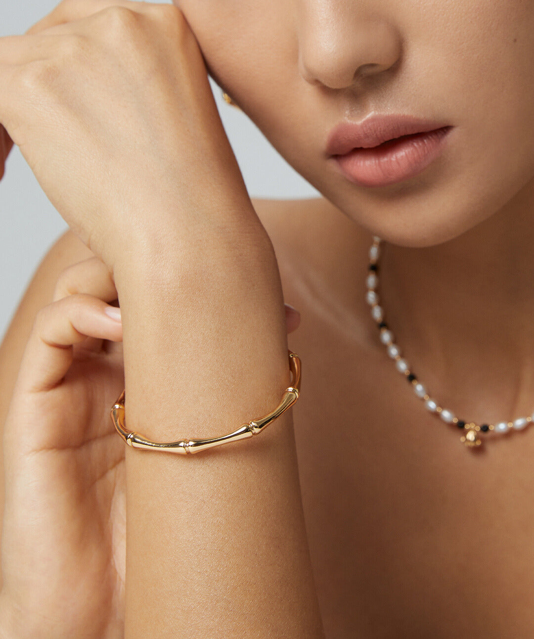 A model showcasing a gold bracelet with a pearl necklace. The bracelet has a unique bamboo texture.