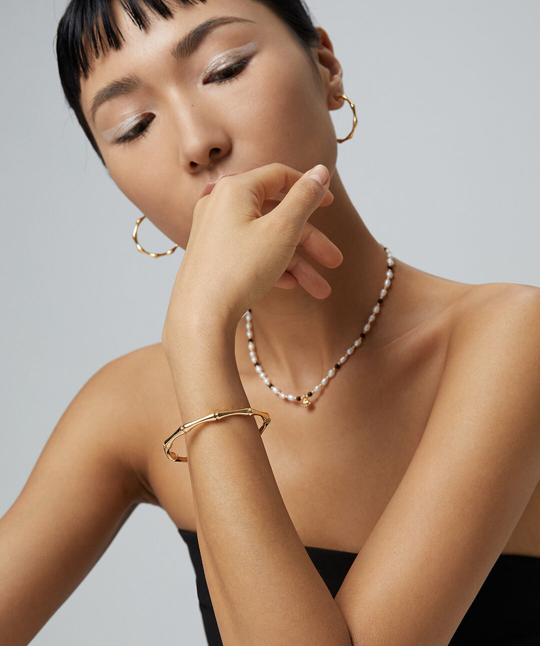 A model showcasing a gold necklace and bracelet, with a stunning gold bangle featuring a bamboo texture.