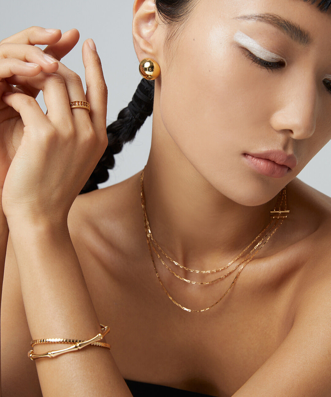 A model showcasing a gold chain and earrings, complemented by a gold bangle with a beautiful bamboo texture, all in matching jewelry.