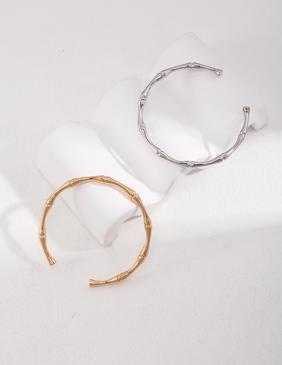 Two bamboo-textured silver and gold bangles on white surface.