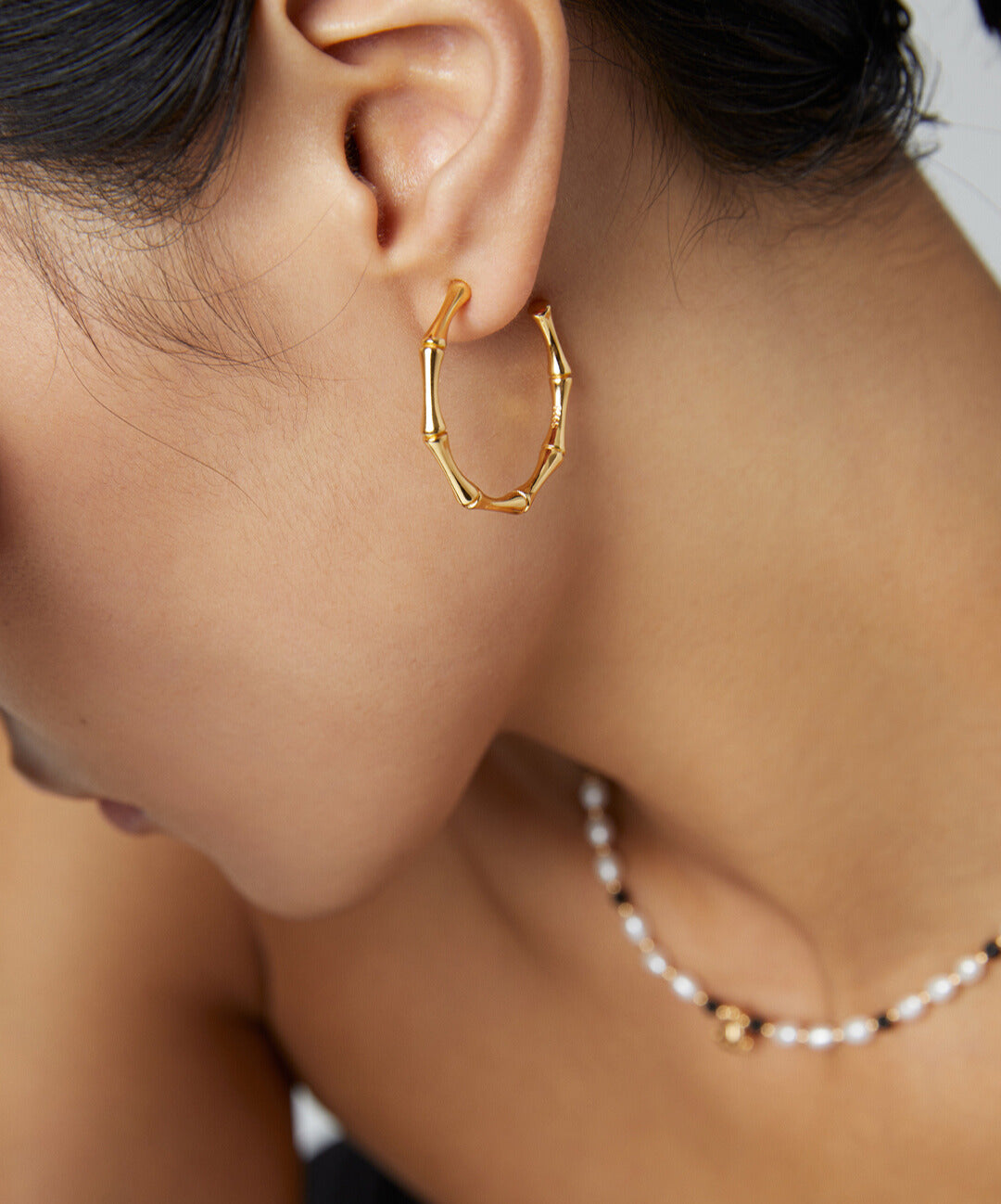 Woman wearing gold bamboo half hoop earrings and necklace.